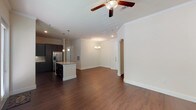This single-story residence is designed with a cohesive, contemporary aesthetic that balances functionality and style. The open-concept living and dining area serves as the heart of the home, featuring rich dark hardwood-style flooring, crown molding, and ceiling fans. A chandelier adds an elegant focal point, while an arched doorway provides a graceful architectural detail. The kitchen is well-equipped with dark espresso cabinetry extending to the ceiling, granite countertops, a subway tile backsplash, and a full suite of stainless steel appliances including a side-by-side refrigerator, range, microwave, and dishwasher. A center island provides additional prep and storage space. The bedrooms are carpeted for comfort, each featuring ceiling fans and windows with blinds that invite natural light. Both walk-in closets offer wrap-around hanging rods and carpeted floors, providing generous storage. The primary bathroom is notably spacious, featuring dark hardwood-style flooring, a double vanity with granite countertops, dark cabinetry, a glass-enclosed shower, and a separate soaking tub with full tile surround. A secondary bathroom includes a tub-shower combination with large-format tile, a granite vanity, and matching dark cabinetry, maintaining a consistent design language throughout.
