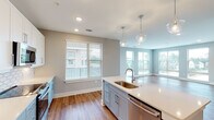 This single-floor residence at 5824 McCrimmon Pkwy in Morrisville, NC, presents a well-designed open-concept layout with contemporary finishes. The kitchen serves as a central highlight, featuring a large island with a undermount sink, crisp white quartz countertops, two-tone cabinetry with white upper and soft blue-gray lower cabinets, a decorative arabesque tile backsplash, stainless steel appliances, and glass pendant lighting. The kitchen flows seamlessly into the living area, where multiple windows allow generous natural light and warm hardwood-style flooring runs throughout the main living spaces. The bedrooms are carpeted and include ceiling fans and windows with exterior views. The primary bathroom offers a walk-in glass shower, a double-sink vanity with white cabinetry and quartz countertop, hardwood-style flooring, and direct access to a spacious walk-in closet with wire shelving. A secondary full bathroom provides a tiled tub-shower combination, a single-sink vanity, and consistent flooring. The neutral gray color palette and clean architectural lines contribute to a cohesive, modern ambiance throughout the entire space.