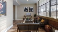 Located at 34 Franklin in Has, New Hampshire, this single-floor unit blends industrial character with refined interior finishes to create a cohesive and inviting living environment. The open-concept layout connects the main living and kitchen areas seamlessly, as seen in the overhead floor plan view, offering a generous sense of space and easy flow throughout.

The living area is a standout feature, anchored by large, multi-pane windows that flood the space with natural light and frame views of the surrounding cityscape. Exposed brick accents and wood-style flooring add warmth and texture, complementing the contemporary furnishings and bold wall art. Recessed lighting and high ceilings further enhance the airy, loft-like atmosphere.

The kitchen is well-appointed with cream-toned cabinetry, granite countertops, and a full suite of stainless steel appliances, including a range, dishwasher, and over-the-range microwave. Wood-style flooring continues throughout, tying the spaces together cohesively.

The bedrooms offer a calm, neutral palette with warm beige walls, plush carpeting, and thoughtful details such as decorative mirrors and framed artwork. The bathroom features wood-style flooring, granite-topped cabinetry, and a full tub-shower combination, providing a clean and functional design.