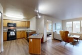 Located at 1140 N 192nd St in Shoreline, WA, this thoughtfully laid-out one-bedroom, one-bathroom residence offers a functional and comfortable living environment across a single floor. The open-concept kitchen and living area serves as the heart of the home, where warm wood cabinetry, black appliances—including a range, microwave, and dishwasher—and a peninsula with counter seating create an efficient and inviting kitchen space. Hardwood-style flooring flows throughout, adding warmth and continuity to the layout. The living room features a large window that brings in natural light and views of the surrounding neighborhood, providing a bright and relaxed atmosphere. A dedicated office space with sliding panel doors and carpeted flooring offers a quiet, flexible area suitable for work or use as a dining nook. The bedroom is a cozy retreat with a sizable sliding-door closet, soft carpeting, and a window that allows in natural light. The full bathroom is spaciously proportioned, outfitted with wood-toned cabinetry, a vanity sink, and a glass-enclosed shower. Three closets throughout the unit provide generous storage. This well-appointed residence combines practical design with comfortable livability in a convenient Shoreline location.