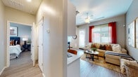 This single-floor residence offers a thoughtfully designed open-concept layout that seamlessly connects the kitchen, dining, and living areas. The kitchen is a standout feature, showcasing crisp white shaker cabinetry, quartz countertops, stainless steel appliances including a range, microwave, and refrigerator, and a central island with bar seating — ideal for casual dining and entertaining. Light wood-style flooring runs throughout, contributing to a clean, cohesive aesthetic.

The living room is bright and inviting, with large windows dressed in bold red curtains that bring warmth and contrast to the neutral palette. A ceiling fan overhead adds comfort, while the open flow from the entry hallway enhances the sense of spaciousness.

Two bedrooms provide comfortable retreats. The primary bedroom features natural light from a large window with blinds, a ceiling fan, and ample space for furnishings. The secondary bedroom similarly benefits from a well-placed window and a relaxed, airy feel.

The bathroom is finished with a white vanity, quartz countertop, wood-style flooring, and a bright window for natural ventilation and light. Throughout the residence, consistent use of neutral tones, modern hardware, and thoughtful finishes create a cohesive and welcoming living environment.