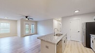 Located at 9924 Cooper Church Dr in Louisville, KY, this 2-bedroom, 2-bathroom apartment offers a thoughtfully designed single-floor layout with modern finishes throughout. The open-concept kitchen and living room serves as the heart of the home, anchored by a granite-topped island with a built-in sink, white shaker cabinetry, and stainless steel appliances including a gas range, microwave, and refrigerator. Light hardwood-style flooring runs throughout the main living areas, adding warmth and continuity. The spacious living room is bathed in natural light from a side window and French doors that open directly onto a private balcony, complemented by a ceiling fan overhead. Both bedrooms feature plush carpeting and generous natural light from large windows. The primary bedroom is notably spacious and includes a walk-in closet outfitted with wire shelving on multiple levels. Each bathroom is finished with granite-topped vanities, light wood-style flooring, and a tub/shower combination with matte black fixtures and hardware, lending a clean, contemporary aesthetic. A dedicated utility room and two closets provide ample storage. The unit's neutral color palette and consistent modern design create a bright, cohesive living environment throughout.
