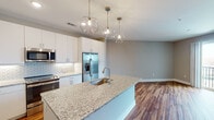 Located at 2815 Capital Blvd in Raleigh, NC, this single-floor unit offers a thoughtfully designed open-concept layout with modern finishes throughout. The kitchen serves as a central highlight, featuring a large granite-topped island with an undermount sink, white shaker-style cabinetry extending to the ceiling, and a geometric patterned tile backsplash. Stainless steel appliances — including a French door refrigerator with ice maker, electric range, and built-in microwave — complete the functional and stylish space. Geometric pendant light fixtures add a contemporary touch above the island.

Warm hardwood-style flooring extends throughout the main living areas, creating a cohesive and inviting atmosphere. The open living area receives natural light and provides direct access to a private balcony through a sliding glass door, offering outdoor views of the surrounding Raleigh area.

The bedroom features plush carpeting and a window fitted with blinds for natural light control. The bathroom is finished consistently with the rest of the unit, showcasing a granite-topped vanity, white cabinetry, and hardwood-style flooring. Neutral gray walls throughout the unit lend a clean, contemporary aesthetic well-suited to modern living.