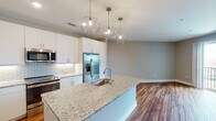 Located at 2815 Capital Blvd in Raleigh, NC, this single-floor unit offers a thoughtfully designed open-concept layout with modern finishes throughout. The kitchen serves as a central highlight, featuring a large granite-topped island with an undermount sink, white shaker-style cabinetry extending to the ceiling, and a geometric patterned tile backsplash. Stainless steel appliances — including a French door refrigerator with ice maker, electric range, and built-in microwave — complete the functional and stylish space. Geometric pendant light fixtures add a contemporary touch above the island.

Warm hardwood-style flooring extends throughout the main living areas, creating a cohesive and inviting atmosphere. The open living area receives natural light and provides direct access to a private balcony through a sliding glass door, offering outdoor views of the surrounding Raleigh area.

The bedroom features plush carpeting and a window fitted with blinds for natural light control. The bathroom is finished consistently with the rest of the unit, showcasing a granite-topped vanity, white cabinetry, and hardwood-style flooring. Neutral gray walls throughout the unit lend a clean, contemporary aesthetic well-suited to modern living.