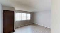 This single-floor space offers a clean and functional layout with a straightforward, practical design. The main living area is finished with light-toned hardwood flooring that lends warmth and a sense of openness to the room. Neutral gray walls create a calm, versatile backdrop suitable for a variety of interior styles and furnishings. A large window fitted with vertical blinds serves as a prominent architectural feature, allowing generous natural light to fill the space while offering privacy control as needed. The textured popcorn ceiling adds a classic touch, and crisp white baseboards provide a clean contrast against the neutral walls. The overall ambiance is bright, open, and move-in ready, with a minimalist character that makes it easy to personalize. The single-floor layout ensures convenient, step-free access throughout, making the space both practical and accessible. This is a straightforward, well-lit unit that provides a solid foundation for comfortable everyday living.