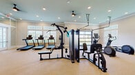 Located at 2150 NW 21st St in Ocala, Florida, this fitness center is a thoughtfully designed, single-floor facility built to support a full range of workout routines. The space is finished with neutral-toned walls, crown molding, and light wood-style flooring throughout, creating a clean and inviting atmosphere. Recessed lighting and ceiling fans ensure the space remains well-lit and comfortable during use.

Large windows along multiple walls flood the interior with natural light, while a glass garage-style door on one side opens the fitness area to outdoor views, enhancing the sense of openness. Wall-mounted televisions provide entertainment options during workouts.

The cardio section is equipped with multiple treadmills, elliptical trainers, and a stationary bike, all arranged to take advantage of the natural light and outdoor sightlines. The strength training area features a multi-function cable machine, a Smith machine with an adjustable bench, and additional cable and functional training stations. Full-length mirrors along one wall expand the visual space and allow for form monitoring during exercises.

Built-in shelving provides organized storage, and sanitation stations are conveniently placed throughout. French doors connect to an adjacent room, offering additional utility. The overall design balances functionality with a polished, modern aesthetic.
