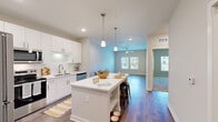 Located at 300 Perigon Dr in Palm Coast, Florida, this one-bedroom, one-bathroom unit offers a well-designed single-floor layout that makes efficient use of its space. The open-concept kitchen is a standout feature, boasting crisp white cabinetry, a subway tile backsplash, stainless steel appliances including a refrigerator, range, and microwave, and a large quartz-topped island with pendant lighting overhead. Recessed lighting and wood-style flooring carry throughout the kitchen and living areas, lending the space a clean, modern aesthetic. The adjoining living and dining area is bright and open, with a ceiling fan and windows that allow natural light to fill the room. The bedroom is carpeted for comfort, features its own ceiling fan, and includes a window with outdoor views. The bathroom is finished with a tiled tub-shower combination, wood-style flooring, and quartz countertops that coordinate with the rest of the unit. A dedicated laundry room houses a full-size top-loading washer and dryer, complete with built-in shelving above for added storage. A separate closet provides additional organization space, completing this thoughtfully laid-out home in Palm Coast.
