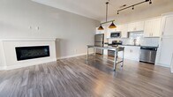 This contemporary apartment showcases a thoughtful design that maximizes space and functionality. The open-concept layout seamlessly integrates the living areas, creating a fluid and airy atmosphere. The kitchen is a standout feature, boasting white cabinetry, stainless steel appliances, and a subway tile backsplash. A central island with pendant lighting serves as both a workspace and casual dining area.

The living room is anchored by a sleek, built-in electric fireplace, adding warmth and sophistication. Large windows and French doors flood the space with natural light and lead to a private balcony. Bedrooms are generously sized with ample closet space, featuring wire shelving systems for optimal organization.

The bathroom continues the modern aesthetic with a floating vanity, large mirror, and glass shower enclosure. Throughout the apartment, neutral tones and wood-look flooring create a cohesive, elegant ambiance. High ceilings and recessed lighting further enhance the sense of spaciousness, making this apartment an ideal urban retreat.