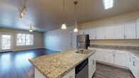 Located at 264 E Pebble Hollow Way in Draper, Utah, this single-floor residence offers a thoughtfully designed open-concept layout that seamlessly connects the kitchen, dining, and living areas. The kitchen is a standout feature, boasting granite countertops throughout, a central island with a double sink and built-in dishwasher, crisp white cabinetry with brushed nickel hardware, and a full suite of stainless steel appliances including a refrigerator, range, and over-the-range microwave. Pendant lighting above the island and a flush skylight panel add both style and practicality to the space. Hardwood-style flooring runs throughout the main living areas, reflecting natural light that pours in through large windows and a glass-panel door. The living room is generously proportioned, featuring a ceiling fan and track lighting, creating a bright and versatile space. The bedrooms are carpeted for comfort, each offering natural light via slatted windows and ceiling fans. The bathroom includes a full soaking tub and shower combination with tiled surrounds and chrome fixtures. Neutral warm tones on the walls throughout give the home a cohesive, welcoming ambiance well-suited for comfortable everyday living.
