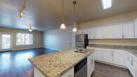 Located at 264 E Pebble Hollow Way in Draper, Utah, this single-floor residence offers a thoughtfully designed open-concept layout that seamlessly connects the kitchen, dining, and living areas. The kitchen is a standout feature, boasting granite countertops throughout, a central island with a double sink and built-in dishwasher, crisp white cabinetry with brushed nickel hardware, and a full suite of stainless steel appliances including a refrigerator, range, and over-the-range microwave. Pendant lighting above the island and a flush skylight panel add both style and practicality to the space. Hardwood-style flooring runs throughout the main living areas, reflecting natural light that pours in through large windows and a glass-panel door. The living room is generously proportioned, featuring a ceiling fan and track lighting, creating a bright and versatile space. The bedrooms are carpeted for comfort, each offering natural light via slatted windows and ceiling fans. The bathroom includes a full soaking tub and shower combination with tiled surrounds and chrome fixtures. Neutral warm tones on the walls throughout give the home a cohesive, welcoming ambiance well-suited for comfortable everyday living.