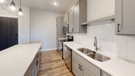 Located at 223 Roberts St N in Fargo, North Dakota, this thoughtfully designed single-floor unit offers a clean, modern aesthetic throughout. The kitchen serves as the centerpiece of the space, showcasing gray shaker-style cabinetry, crisp white quartz countertops, and a herringbone-patterned tile backsplash. A large kitchen island provides generous prep and gathering space, illuminated by a trio of geometric pendant lights. Stainless steel appliances — including a range, built-in microwave, dishwasher, and refrigerator — complete the well-equipped culinary setup. The kitchen flows seamlessly into an open living area with rich hardwood-style flooring and natural light streaming in through a large window, creating a bright and welcoming atmosphere. A dedicated bedroom features the same durable flooring, neutral wall tones, and a window that brings in natural light, offering a versatile and comfortable retreat. The bathroom is finished with large-format marble-look porcelain tile flooring, a dual-sink vanity with gray cabinetry, a walk-in shower, and clean white fixtures, lending the space a polished, spa-like feel. Throughout the unit, recessed lighting, black hardware accents, and neutral color tones contribute to a cohesive contemporary design.