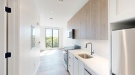 Unit 317 at 282 Bremen Street in Boston's East Boston neighborhood is a thoughtfully designed studio offering a clean, modern aesthetic throughout. The open-concept layout seamlessly connects the kitchen and living area, maximizing the efficient use of space. The kitchen features warm wood-toned upper cabinetry, white lower cabinets, sleek white quartz countertops, a stainless steel range, and a matte black gooseneck faucet over an undermount sink — a refined combination of style and function. Light wood-style flooring runs throughout, brightening the interior and adding warmth. The living area is bathed in natural light, thanks to expansive floor-to-ceiling windows framed in black that frame treetop views of the surrounding neighborhood. A dedicated closet provides practical storage, while the hallway leads to a full bathroom finished with white subway-style tile, a glass-enclosed walk-in shower, and gunmetal hardware for a contemporary touch. In-unit laundry is also present, adding everyday convenience. The crisp white walls, recessed lighting, and modern fixtures give the space a fresh, move-in-ready feel, making this studio an ideal option for those seeking stylish urban living in Boston.