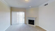 This single-floor residence offers a welcoming and well-appointed living space designed with both comfort and functionality in mind. The main living area is a standout, featuring soft wall-to-wall carpeting that adds warmth underfoot and elegant crown molding that runs along the perimeter of the ceiling, lending the room a refined, polished character. A classic fireplace with a white painted mantel serves as a natural focal point, providing a charming centerpiece that enhances the room's cozy ambiance. Large sliding glass doors dressed with vertical blinds line one wall, allowing an abundance of natural light to flood the interior while offering easy access to the outdoors and views of the surrounding greenery. The neutral, warm-toned walls provide a versatile backdrop that complements a variety of décor styles. Recessed and flush-mounted ceiling lighting ensures the space is well-lit throughout the day and into the evening. The overall atmosphere is calm and inviting, with a clean, move-in-ready aesthetic that balances classic architectural details with practical everyday living. This space is ideal for those seeking a comfortable and characterful home environment.