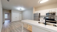 Located at 1345 Wenlon Dr in Murfreesboro, Tennessee, this single-floor residence offers a thoughtfully designed layout that makes efficient use of its space. The open-concept kitchen serves as a central hub, outfitted with white shaker-style cabinetry, a classic subway tile backsplash, and a full suite of stainless steel appliances including a refrigerator, electric range, and microwave. A peninsula with a quartz-style countertop and an undermount sink with a matte black faucet provides additional workspace and a natural divider between the kitchen and the living area. Light wood-look luxury vinyl flooring runs consistently throughout the unit, lending a clean and cohesive aesthetic. The living area features double closets with paneled doors, offering generous storage. The bedroom is bright and airy, with multiple windows fitted with horizontal blinds that allow for natural light and privacy control, complemented by a ceiling fan. The bathroom is cleanly finished with white cabinetry, a single-sink vanity with a solid countertop, and a tiled shower-tub combination, all accented by matte black hardware. Neutral warm-gray wall tones and white trim work throughout the space create a modern yet inviting atmosphere well suited for everyday living.