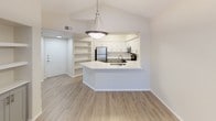 This well-appointed single-floor residence showcases a thoughtful open-concept layout with a warm, neutral color palette throughout. The living room serves as the heart of the home, featuring soaring vaulted ceilings, a ceiling fan, large windows that flood the space with natural light, and a tile-surround fireplace that adds a classic focal point. Light wood-look flooring flows through the main living and kitchen areas, enhancing the airy feel.

An elegant arched passageway framed by decorative columns connects the living area to the kitchen, where white upper cabinetry and sage-toned lower cabinets pair with a subway tile backsplash. The kitchen is equipped with stainless steel appliances and anchored by a peninsula featuring a white countertop and an undermount sink—ideal for both meal prep and casual dining. Built-in shelving near the entryway provides convenient display and storage space.

The bedrooms are carpeted for comfort, with the primary suite offering vaulted ceilings, a ceiling fan, and expansive windows with vertical blinds. One bedroom includes direct outdoor access via a glass-panel door. The bathrooms are finished with wood-look tile flooring, white countertops, and brushed nickel fixtures. One bath includes a walk-in shower, while another features a tub-shower combination.