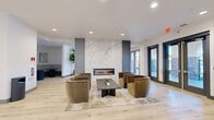 Located at 3200 Pleasant Grove Blvd in Roseville, California, this generously sized community room offers a thoughtfully designed, open-plan gathering space across a single floor. The interior is finished with light hardwood flooring throughout, crisp white walls, and recessed lighting that creates a bright, welcoming ambiance.

The main lounge area is anchored by a stunning floor-to-ceiling marble surround fireplace, serving as a dramatic focal point. Plush velvet swivel chairs and a sleek coffee table invite relaxed conversation, while large glass doors open to outdoor views, flooding the space with natural light. A distinctive arched window in a separate seating nook further enhances the architectural character of the room, framing courtyard views beautifully.

Additional seating zones include a curved sectional sofa paired with leather accent chairs and wall-mounted television, as well as a casual lounge corner furnished with oversized leather bean bag chairs and built-in cabinetry in a sophisticated slate-blue finish. Decorative potted plants add warmth and life throughout.

The games area is equipped with a full-size pool table and a shuffleboard table, both in rich wood tones, complemented by wall-mounted televisions and cue storage. The overall design balances modern sophistication with comfortable, community-oriented functionality, making this an ideal venue for social gatherings and recreation.