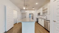 Located at 10440 Daybreak Trail Ct in Sun City Center, Florida, this single-story home presents a clean, contemporary design with a bright, open-concept floor plan. The kitchen serves as the centerpiece of the living area, showcasing a large island with speckled granite countertops, crisp white cabinetry extending to the ceiling, and a full suite of stainless steel appliances including a refrigerator, range, microwave, and dishwasher. A white subway tile backsplash and globe pendant lighting add refined detail, while wood-look flooring flows seamlessly into the adjacent living area. The living space is well-lit by multiple windows fitted with horizontal blinds, and a ceiling fan enhances comfort throughout. Bedrooms feature plush carpet flooring, natural light from windows, and generous closet space with wire shelving systems, including a spacious walk-in closet. The bathrooms maintain the home's modern aesthetic with white vanity cabinetry, granite-topped counters, undermount sinks, and wood-look flooring. A dedicated laundry area accommodates a full-size washer and dryer side by side. The overall ambiance is fresh, neutral, and move-in ready.
