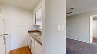 This single-floor residence offers a practical and comfortable layout across two bedrooms, two bathrooms, a hallway, and a dedicated closet. The kitchen is efficiently designed with white cabinetry, dark laminate countertops, a double stainless steel sink, and a full-size refrigerator. Wood-look flooring runs through the kitchen, adding warmth and easy maintenance to the space. The kitchen opens conveniently toward the living area, which features plush carpeting, neutral-toned walls, a textured ceiling, and a sliding glass door that leads to a private balcony, allowing natural light to fill the room. Both bedrooms are carpeted and equipped with ceiling fans with integrated lighting. The primary bedroom is generously proportioned, offering ample space for furnishings, while the second bedroom features a window that brings in additional natural light. Each bathroom includes a tub-shower combination and wood-look flooring, with vanities featuring dark countertops consistent with the kitchen's design aesthetic. The hallway connects the rooms efficiently, contributing to the overall cohesive flow of the layout. Throughout the residence, a consistent neutral color palette and textured ceilings create a clean, understated ambiance.