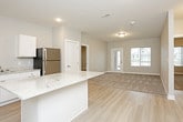 This single-floor residence is designed with a clean, contemporary aesthetic throughout, utilizing a neutral gray-and-white palette that creates a cohesive and calming atmosphere. The open-concept living area features light-toned luxury vinyl plank flooring that flows seamlessly toward the kitchen, while plush carpet defines the living space and bedrooms.

The kitchen serves as a functional centerpiece, equipped with crisp white cabinetry, light granite countertops, a central island with additional granite surface space, and a full suite of stainless steel appliances including a range, microwave, dishwasher, and refrigerator. Recessed lighting illuminates the space effectively.

The living area is bright and spacious, with a glass door and adjacent window that invite natural light and provide views of the surrounding neighborhood. Bedrooms are carpeted and offer generous proportions, with windows bringing in additional daylight.

The primary bathroom features light hardwood-style flooring, a walk-in shower, a granite-topped vanity, and direct access to a walk-in closet fitted with wire shelving. A second full bathroom includes a tub-shower combination with granite vanity details. A dedicated laundry room houses a full-size top-loading washer and dryer with overhead wire shelving for storage.