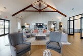 Located in Bonita Springs, Florida, this thoughtfully designed single-story clubhouse offers an expansive, open-concept layout finished with warm hardwood flooring throughout. The centerpiece of the space is the dramatic vaulted ceiling adorned with rich, dark exposed wood beam trusses and an eye-catching branch-inspired chandelier, lending a refined yet welcoming atmosphere to the main lounge area. Generously sized windows and sets of black-framed French doors flood the interior with natural light while providing direct access to an outdoor patio area.

The main gathering area features multiple stylish seating arrangements, creating versatile spaces for relaxation and socializing. A cozy fireplace nook with floor-to-ceiling arched detailing and flanking windows serves as an intimate retreat within the larger room. A dedicated game area accommodates a full-size shuffleboard table, complemented by vibrant curated artwork on the walls.

The kitchenette area includes white cabinetry, stainless steel appliances, a gray tile backsplash, and a dining table beneath an elegant pendant chandelier. A separate conference room features a large wood table, ergonomic seating, built-in cabinetry, a mounted display screen, and textured accent wall, making it ideal for professional meetings or community gatherings.