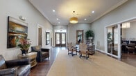 Located at 3600 Winthrop Dr in Lexington, Kentucky, this single-story community clubhouse offers a well-appointed collection of amenity spaces designed for comfort, leisure, and active living. The welcoming entrance foyer features rich hardwood flooring, crown molding, elegant pendant lighting, and refined furnishings that set an upscale tone throughout.

The main lounge area is a standout space, anchored by a dramatic floor-to-ceiling stacked stone fireplace with a wall-mounted TV above. Large glass French doors open directly to an outdoor patio overlooking a serene pond with a fountain, flooding the room with natural light. Adjacent seating areas provide comfortable gathering spaces with tasteful décor including curated artwork and soft, neutral furnishings.

A dedicated lounge nook features hardwood floors, leather club chairs, a beverage station, and a mounted TV, offering a relaxed setting for socializing. Private meeting or office rooms branch off from this area, appointed with leather seating and decorative accents.

The fitness center is comprehensively equipped, offering treadmills, cable machines, free weights, and adjustable benches across two well-lit rooms with ceiling fans, floor-to-ceiling mirrors, and crown molding details.

A private screening room rounds out the amenities, featuring rows of leather theater-style seating with cup holders and a large projection screen, providing a true cinematic experience on-site.