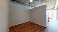Located at 2200 Market Street in Denver's vibrant Curtis Park neighborhood, this urban loft-style unit showcases a compelling blend of industrial and modern design. The space is defined by its exposed concrete ceilings with visible ductwork and piping, which lend a distinctive warehouse aesthetic throughout. Hardwood flooring runs throughout the main living and kitchen areas, adding warmth to the raw industrial backdrop.

The kitchen is a functional highlight, featuring warm wood cabinetry, granite countertops, and a full suite of stainless steel appliances including a refrigerator, range, microwave, and dishwasher. A peninsula with a double stainless steel sink and pendant lighting above serves as both a workspace and a casual gathering point. Track lighting on the concrete ceiling adds to the kitchen's modern utility. French doors lead from the living area to a balcony, offering open views of the Denver skyline and filling the space with natural light.

The bedroom area features rich hardwood floors, a ceiling fan, and exposed concrete ceiling details consistent with the loft's overall aesthetic. The bathroom is finished with tile flooring, a tub-shower combination with tiled surround, a wood vanity with granite countertop, and a large mirror — clean and well-appointed. This single-floor unit delivers a cohesive urban living experience in the heart of Denver.