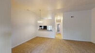 This single-floor residence offers a thoughtfully designed open layout that promotes a natural flow between living and dining areas. The main living space features plush carpeting, soaring vaulted ceilings, and a pendant chandelier that adds a touch of elegance above the dining area. A pass-through window connects the living space to the kitchen, enhancing the open feel while maintaining a sense of structure.

The kitchen is well-appointed with white raised-panel cabinetry, rich dark granite countertops, tile flooring, and a full suite of stainless steel appliances including a refrigerator, electric range, over-the-range microwave, and dishwasher. A skylight above the kitchen provides additional natural illumination.

The living room is a standout space, highlighted by a bay window arrangement that fills the room with natural light and frames views of surrounding greenery. A classic fireplace with a gold-trimmed surround anchors one wall, creating a warm and inviting focal point.

Bedrooms are carpeted and bright, with large windows that invite natural light. The bathroom includes tile flooring with granite-topped vanity, a full soaking tub and shower combination, and brushed nickel fixtures. Throughout, the clean white walls and consistent finishes lend a cohesive, move-in-ready aesthetic.