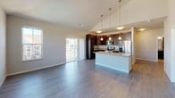 Located on Nobel Drive in Fitchburg, Wisconsin, this single-floor unit offers a thoughtfully designed open-concept layout that seamlessly connects the living, dining, and kitchen areas. The kitchen is a standout feature, outfitted with rich dark espresso cabinetry, stainless steel appliances including a range, microwave, and refrigerator with water dispenser, and light-toned countertops. A central island with pendant lighting above anchors the space, while wood-style flooring extends throughout the main living area. Vaulted ceilings in the living room enhance the sense of openness, and a sliding glass door leads to a private balcony with views of the surrounding neighborhood. The bedrooms are generously sized, featuring plush carpeting, large windows that invite abundant natural light, and outdoor views. One bedroom includes a ceiling fan for added comfort. The bathrooms are finished in a clean, neutral palette — one featuring a full tub/shower combo and dark wood vanity, and another with a sleek vanity, modern light fixture, and framed mirror. Throughout the unit, a consistent design language of dark cabinetry, neutral walls, and warm flooring creates a cohesive and contemporary living environment.