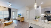 This well-appointed single-floor residence offers a thoughtfully designed open-concept layout that seamlessly connects the kitchen, dining, and living areas. The kitchen is equipped with stainless steel appliances, gray shaker-style cabinetry, a subway tile backsplash, and granite countertops that extend to a breakfast bar with elegant pendant lighting overhead. Wood-style flooring flows throughout the space, adding warmth and continuity.

The living area is bright and airy, benefiting from large windows with blinds and access to an exterior door, allowing for ample natural light. A second living or sitting room features a distinctive patterned accent wall, arched display cabinetry, and a ceiling fan, creating a cozy yet sophisticated retreat.

Both bedrooms are generously sized, each with ceiling fans, windows with natural light, and stylish accent walls. The primary bedroom connects to a well-sized walk-in closet with wire shelving systems offering flexible storage. The en-suite primary bathroom features a dual-sink granite vanity, undermount sinks, gray cabinetry, and a glass-enclosed walk-in shower. A second full bathroom mirrors the refined finishes with a granite-topped vanity and hardwood-style flooring, rounding out this polished and functional residence.