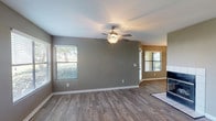 This single-floor residence offers a thoughtfully designed layout with a clean, contemporary aesthetic throughout. The open living area is anchored by rich wood-look flooring, neutral gray walls, and a ceiling fan that enhances both comfort and style. Multiple windows fitted with blinds allow generous natural light to fill the space while offering outdoor views of surrounding greenery. A tile-surround fireplace serves as a standout focal point in the living area, adding warmth and character.

The kitchen is efficiently arranged in an L-shaped layout, featuring crisp white cabinetry, light countertops, and a full suite of black appliances including a refrigerator, electric range, built-in microwave, and dishwasher. The wood-look flooring continues seamlessly into this space, maintaining a cohesive look throughout the common areas.

The bedroom is finished with plush carpeting, a ceiling fan with light fixture, and a window that brings in natural light. The bathroom is well-appointed with a wide vanity topped with a speckled countertop, white cabinetry, a large mirror, a tub-shower combination with tile surround, and wood-look flooring that ties the room together. The entry area provides a welcoming transition into the home. Overall, this residence presents a functional and comfortable living environment with consistent finishes throughout.
