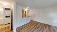 Located at 2505 Quail Ridge Drive in Plainsboro, New Jersey, this studio unit offers a practical and well-appointed single-floor layout. The main living area is bright and open, featuring wood-style plank flooring that runs throughout and neutral white walls that enhance the sense of light and space. Two windows fitted with horizontal blinds allow natural light to filter in while providing views of surrounding greenery. A wall-mounted HVAC unit ensures year-round climate control.

The kitchen is defined by a pass-through opening with a granite countertop ledge, creating a natural division between the living space and cooking area. Inside, grey shaker-style cabinetry provides ample storage, complemented by granite countertops and stainless steel appliances including an electric range, over-the-range microwave, refrigerator, and dishwasher.

The bathroom is clean and functional, featuring light tile flooring, a full tub-shower combination with a chrome curtain rod, a toilet, and a single vanity with a white countertop and mirror. The overall aesthetic throughout the unit is minimal and move-in ready, with a cohesive neutral palette.