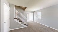 Located at 10932 Richards Ct in Lenexa, Kansas, this three-floor home offers a well-organized layout with consistent finishes throughout. The main level features light wood-look flooring and a modern kitchen equipped with white shaker-style cabinetry, granite-look countertops, a subway tile backsplash, and black Whirlpool appliances including a range with over-the-range microwave and a refrigerator. A second kitchen or kitchenette area is also present, outfitted with white cabinetry and black appliances, suggesting a lower-level in-law suite or additional living space. A classic staircase with white spindle balusters and carpeted treads connects the floors, accented by a decorative angled wall feature at the landing. The upper levels showcase generously sized rooms with plush wall-to-wall carpeting, neutral gray walls, and textured ceilings. Each room benefits from natural light provided by windows with blinds. One bedroom includes a ceiling fan, while others offer ample open floor space. The clean, neutral palette and consistent trim work throughout the home provide a versatile canvas well-suited for a variety of interior styles.