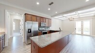 This thoughtfully designed single-story home offers four bedrooms and three bathrooms across a well-utilized floor plan. The kitchen serves as the heart of the home, showcasing rich cherry wood cabinetry, granite countertops, a large center island with a built-in sink, and a full suite of stainless steel appliances, including a French door refrigerator, electric range, microwave, and dishwasher. A mosaic tile backsplash adds texture and visual interest throughout the cooking space. Adjacent to the kitchen, the dining area features a striking coffered ceiling with a geometric chandelier and French doors that open to an outdoor space, flooding the area with natural light. The primary bedroom is generously proportioned, highlighted by a tray ceiling with crown molding and a ceiling fan. The remaining bedrooms are finished with plush carpeting and crisp white trim. The bathrooms are elegantly appointed with granite-topped wood vanities and large-format tile flooring. Additional spaces include two closets, a hallway, and light wood-toned flooring that flows consistently through the main living areas, enhancing the home's cohesive, modern aesthetic.