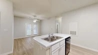 This single-story home at 6204 Crow Lane in Austin, TX is designed with a clean, neutral palette and an open, functional layout. The kitchen serves as a central hub, featuring a peninsula island with a double-basin sink, white cabinetry, white countertops, a subway tile backsplash, and black appliances including a refrigerator, range, and over-the-range microwave. A skylight panel above the kitchen enhances natural brightness throughout the space.

The kitchen opens directly to the living area, which is finished with light wood-style flooring and includes a ceiling fan overhead. French doors in the living space invite natural light and provide outdoor access. A separate room with matching light flooring offers flexible use as a dining area or home office.

The bedrooms feature plush carpet flooring and ceiling fans, with generous windows fitted with horizontal blinds that allow for adjustable natural light. The bathroom is finished with tile flooring and includes a single-sink vanity with white cabinetry, a large mirror, and a tub-shower combination with tile surround. Throughout the home, neutral tones, clean lines, and consistent finishes create a cohesive and move-in ready atmosphere.