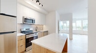 Located at 1600 James Naismith Dr in Ottawa, Ontario, this modern 2-bedroom, 1-bathroom unit offers a thoughtfully designed open-concept layout with a clean, contemporary aesthetic throughout. Light-toned hardwood flooring flows seamlessly across the entire space, complementing the crisp white walls and creating a bright, cohesive atmosphere.

The kitchen is a standout feature, equipped with stainless steel appliances including a refrigerator, electric range, over-the-range microwave, and dishwasher. A central island with a quartz countertop and warm wood cabinetry below provides additional workspace and storage, while white upper cabinets and a neutral subway tile backsplash complete the refined look. Track lighting overhead adds a modern touch.

The living area benefits from expansive floor-to-ceiling windows that flood the space with natural light and offer open outdoor views. Both bedrooms are well-proportioned with large windows, and the primary bedroom includes direct access to a dedicated closet. The bathroom features a soaker tub with a full-height vertical white tile surround, matte black fixtures, and hexagonal floor tile, delivering a clean and stylish finish. The unit also includes a hallway closet, adding practical storage to this well-appointed home.