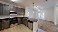 This single-story residence is thoughtfully designed with an open-concept layout that connects the kitchen and living areas seamlessly. The kitchen serves as a functional centerpiece, showcasing dark granite countertops, gray cabinetry, and a full suite of stainless steel appliances, including a refrigerator, range, microwave, and dishwasher. A peninsula with an integrated sink and pendant lighting above adds both style and utility, while light wood-look flooring grounds the space with a clean, contemporary aesthetic. The living area extends naturally from the kitchen, featuring a ceiling fan and access to an outdoor balcony through glass-paned doors, allowing for ample natural light.

The bedrooms are generously proportioned, each finished with plush carpeting, ceiling fans, and windows fitted with blinds that offer outdoor views. At least one bedroom includes a walk-in closet with built-in shelving. The two bathrooms are finished with dark wood vanities topped with granite-style countertops and light wood flooring. One bathroom features a stand-alone shower, while the other offers a shower-tub combination, both outfitted with brushed nickel fixtures. Throughout the residence, neutral tones and consistent finishes create a cohesive and inviting atmosphere.