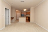This single-floor space is designed with a practical, straightforward layout that maximizes functionality. The kitchen serves as a central feature, equipped with warm honey-toned wood cabinetry offering ample upper and lower storage. Black appliances, including a range and over-the-range microwave, complement the granite-look countertops. A peninsula breakfast bar extends into the adjacent living area, creating a natural transition between the two spaces and providing additional prep or dining surface. The flooring in the kitchen and living area transition between hardwood-style flooring and plush neutral carpeting, respectively, adding texture and comfort throughout.

The living area is open and spacious, benefiting from crown molding details that lend a polished finish to the room. Natural light filters in through a window, brightening the neutral beige walls. The bedrooms are carpeted and generously proportioned, each featuring clean, bare walls with ample room for furnishings. One bedroom includes a window with blinds that allows natural light in, while a six-panel white door provides access to the adjoining hallway. Overall, the space maintains a neutral, move-in-ready palette throughout.