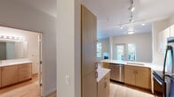Located at 25796 SW Canyon Creek Rd in Wilsonville, Oregon, this well-appointed single-floor unit offers a thoughtfully designed layout with modern finishes and a bright, welcoming ambiance. The open-concept kitchen is outfitted with light wood cabinetry, white quartz countertops, stainless steel appliances including a range, microwave, and dishwasher, and track lighting overhead — all set atop light hardwood-style flooring that flows throughout the main living areas. A peninsula provides additional prep space and naturally connects the kitchen to the living area. The living room is a standout, featuring a corner fireplace with a clean white surround, multiple windows that invite abundant natural light, and a glass door opening to a private balcony with views of lush greenery. A ceiling fan adds comfort to the space. The bedroom is carpeted for warmth and comfort, features its own ceiling fan, and receives natural light through a large window. The bathroom is clean and functional, with a quartz-topped vanity, a tiled soaking tub and shower combination, and hardwood-style flooring. Crown molding and neutral wall tones throughout lend the space a polished, cohesive feel.