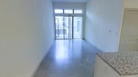 This contemporary single-floor space showcases a clean, minimalist design that blends urban functionality with modern aesthetics. The open-concept layout is anchored by sleek polished concrete floors that reflect natural light throughout, giving the interior a bright and airy quality.

The main living area is defined by a floor-to-ceiling sliding glass door flanked by a transom window above, flooding the space with abundant natural light and providing direct access to a private balcony with metal railing. The outdoor views reveal a surrounding urban environment, ideal for those who appreciate a connected city atmosphere.

The walls are finished in a smooth, neutral tone that complements the industrial character of the concrete flooring, creating a versatile canvas ready for personalization. A partial view of the kitchen area reveals granite countertops, hinting at quality material selections that continue throughout the unit.

Overall, the space exudes a modern, urban sensibility with an emphasis on open space, natural light, and durable, high-quality materials. The single-floor layout ensures easy accessibility and a seamless flow between areas, making it a practical and stylish option for contemporary living.