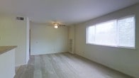 This single-floor space offers a clean, functional layout designed to maximize comfort and usability. The main living area is finished with wall-to-wall carpeting in a neutral tone, creating a soft and welcoming atmosphere throughout. Light-colored walls contribute to an airy, open feel, while a ceiling fan with an integrated light fixture provides both ventilation and overhead illumination.

A standout feature of this room is the built-in shelving unit recessed into the wall, offering practical display or storage space without occupying additional floor area. Natural light flows generously into the space through a large window fitted with horizontal blinds, allowing for easy light control and privacy as needed.

The overall ambiance is understated and versatile, providing a blank canvas that adapts well to a variety of furnishing styles. The neutral palette of the walls, ceiling, and flooring creates a cohesive and harmonious environment. The space is well-suited for everyday living, offering a straightforward and practical floor plan that makes efficient use of every square foot. Its simple, clean design ensures ease of maintenance while remaining inviting and comfortable for its occupants.