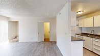 This two-story unit is designed with a clean, functional layout that maximizes usable space across both levels. The main level features a generously sized living area finished with light wood-style laminate flooring and a textured ceiling. Natural light filters in through a sidelight window flanking the front entry door, while a ceiling fan adds comfort to the space. Vertical blinds cover a sliding door, offering access to the exterior. A half-wall partition separates the living area from the galley-style kitchen, which is equipped with white cabinetry, dark laminate countertops, a stainless steel sink, a white electric range, and a full-size refrigerator. Ample upper and lower cabinet storage runs the full length of the kitchen. A hallway off the main living area provides access to a bathroom and staircase leading to the upper level. The bathroom features a white vanity with dark countertop, a framed mirror, a wall-mounted light bar, and a tub-shower combination. The bedrooms are carpeted and receive natural light through standard windows. The primary bedroom includes dual closets, while the secondary bedroom offers a single closet. Both bedrooms feature textured ceilings consistent with the rest of the unit.