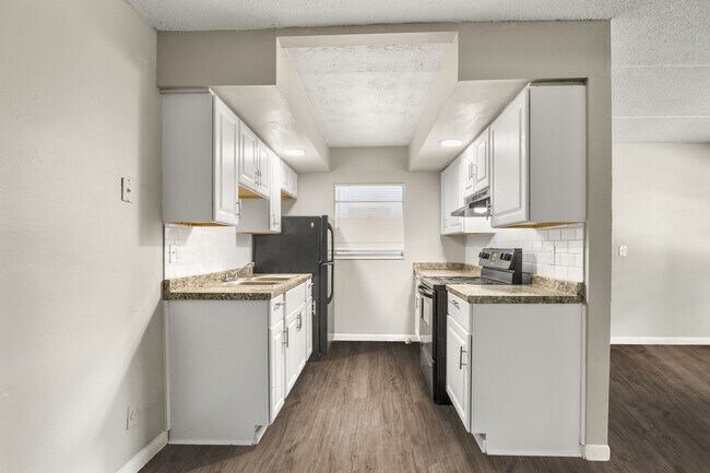 Encantadora cocina con elegantes electrodomésticos negros, armarios blancos y un acogedor suelo de madera. - Alderman Park Apartments