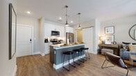 This well-appointed single-floor residence offers a thoughtfully designed open-concept layout that seamlessly connects the kitchen, dining, and living areas. The kitchen is a standout feature, showcasing crisp white shaker cabinetry, granite countertops, a full suite of stainless steel appliances, and a classic subway tile backsplash. A generously sized center island with a two-tone finish provides ample seating for multiple bar stools, making it an ideal hub for casual dining and entertaining. Industrial-style pendant lights hang above, adding a contemporary touch.

The living area is warm and inviting, bathed in natural light from large French doors that open to an outdoor patio, offering views of the surrounding greenery. A ceiling fan and warm-toned flooring running throughout the space contribute to a comfortable, cohesive ambiance.

The bedroom is a tranquil retreat, featuring large windows dressed with elegant curtains and blinds, hardwood-style flooring, and a serene neutral color palette. The bathroom is finished with granite countertops, white cabinetry with matte black hardware, and a well-appointed vanity.

A sliding barn door adds a charming, modern farmhouse detail, while in-unit laundry and recessed lighting complete this polished and functional residence.
