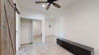 This single-floor unit offers a thoughtfully designed interior that balances contemporary updates with distinctive architectural character. Light wood-style flooring runs throughout the space, creating a warm and cohesive feel across every room.

The main living area is bright and open, featuring a ceiling fan with recessed lighting and clean white walls that enhance the sense of space. A sliding mirrored closet provides generous storage, while the layout flows naturally toward the entry.

The kitchen is a standout area, showcasing an exposed red brick accent wall that adds warmth and texture to the otherwise modern design. White shaker-style cabinetry with dark countertops lines one wall, complemented by black appliances and a pendant light overhead. A rustic sliding barn door connects the kitchen area to the living space, adding a charming farmhouse-inspired touch. A window above the sink brings in natural light and an outdoor view of the surrounding neighborhood.

A separate room with its own exposed brick wall and large double-hung windows offers additional natural light and street views, with a wall-mounted heating unit included for comfort.

The bathroom is clean and bright, finished in white tile with wood-style flooring. It includes a full soaking tub with an overhead shower, a white vanity with chrome fixtures, and a window with blinds for natural ventilation and light.