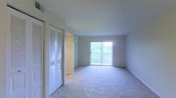 This single-floor residence offers a clean, functional layout designed for comfortable living. The main living area is highlighted by soft, wall-to-wall carpeting that adds warmth underfoot, while neutral-toned walls create a calm and versatile backdrop throughout. A large sliding glass door floods the space with natural light and frames a lush, green outdoor view, giving the room an open and airy feel. The door provides direct access to an outdoor area, enhancing the sense of connection to the surrounding environment. Overhead, a smooth ceiling with a visible HVAC vent ensures year-round climate comfort. A set of bifold louvered closet doors lines one wall, offering generous built-in storage — a practical feature that contributes to the overall tidiness and organization of the space. A hallway visible adjacent to the closet suggests additional rooms beyond the main living area. The overall ambiance is light, understated, and move-in ready, with a straightforward design that allows residents to personalize the space to their own taste. The combination of natural light, neutral finishes, and ample storage makes this a practical and inviting single-level home.