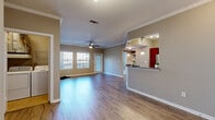 This single-floor residence offers a thoughtfully designed open-concept layout that seamlessly connects the main living areas. The spacious living room is finished with warm hardwood-style flooring, crown molding, and a ceiling fan, while multiple windows invite an abundance of natural light and outdoor views. Crown molding detail adds a refined architectural touch throughout the main living space.

The kitchen is a functional highlight, featuring rich dark-wood cabinetry, granite countertops, stainless steel appliances including a refrigerator, electric range, and built-in microwave, as well as a raised breakfast bar illuminated by elegant pendant lighting. A pass-through opening connects the kitchen to the living area, reinforcing the open and airy feel of the space.

The bedrooms offer plush carpeted flooring and ceiling fans, providing a comfortable and quiet retreat. One bedroom includes direct access to a bathroom, which features a vanity with dark-wood cabinetry, granite countertops, and hardwood-style flooring. A walk-in closet adds practical storage to the layout.

Additional features include an in-unit laundry area and a welcoming entryway. Throughout the residence, neutral warm-toned walls and consistent finishes create a cohesive and inviting ambiance.