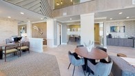 This single-floor space makes an immediate impression through its dramatic architectural design, highlighted by soaring floor-to-ceiling glass curtain walls that flood the interior with abundant natural light and offer expansive views of the surrounding streetscape. The entry lobby sets a refined tone with its double-height ceiling, sheer drapery panels framing the oversized windows, and polished large-format tile flooring that transitions smoothly throughout the space.

A comfortable lounge area near the entrance features upholstered accent chairs, sleek console tables, and sculptural décor accents, creating a welcoming atmosphere for visitors. Moving further into the space, a seating area with plush gray upholstered chairs and a round dining table serves as an informal gathering or meeting zone, complemented by warm wood-toned wall panels and a statement art piece above.

A reception desk anchors the interior, positioned adjacent to glass-enclosed private offices that offer transparency while maintaining separation. A beverage station with cabinetry and mounted display screens adds a functional amenity corner. The angled wood-slat ceiling detail and contemporary chandelier contribute architectural character, while the cohesive neutral palette of grays, warm woods, and soft textures lends the overall space a polished, professional ambiance.