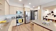 Located at 1910 S Union St in Anaheim, California, this single-floor residence offers a thoughtfully designed layout with a contemporary aesthetic and cohesive design language. The kitchen is a standout feature, showcasing light wood cabinetry, dark countertops, stainless steel appliances including a gas range, built-in microwave, and a large side-by-side refrigerator. A kitchen island with pendant lighting provides additional prep space and casual seating, while wood-look flooring ties the area seamlessly into the rest of the home. An in-unit stacked washer and dryer add everyday convenience. The living area is bright and welcoming, with a ceiling fan, large windows dressed in layered curtains, and access to adjoining rooms. A creative flex room serves as an inspiring multipurpose space, featuring a dramatic ornate wall mural, abundant natural light, and ample room for artistic or work-from-home use. The bedroom is generously proportioned, accommodating a four-poster bed, and connects directly to a walk-in closet for ample storage. The bathrooms are finished with modern vanities, wood-look flooring, and clean tile surrounds. Throughout the residence, a consistent palette of neutral tones, yellow accents, and dark trim details creates a polished, design-forward atmosphere.