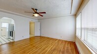 Located at 2651 NW Upshur St in Portland, Oregon, this single-floor unit offers a thoughtfully arranged layout comprising a living room, kitchen, and two bathrooms. The living room is a welcoming, light-filled space showcasing warm hardwood floors that run throughout, crisp white walls, and a textured ceiling accented by a classic wood-blade ceiling fan with integrated lighting. Natural light filters in through windows and a glass-paned exterior door, adding to the bright, airy feel of the room. A graceful arched doorway connects the living area to the kitchen, lending a charming architectural detail to the space. The galley-style kitchen features black-and-white octagonal tile flooring — a timeless design element that continues into the bathrooms — white cabinetry, open shelving, a stainless steel sink, and a dark stone-look countertop with a subtle backsplash. Appliances including a full-size refrigerator are in place. The bathrooms carry through the vintage-inspired aesthetic with matching tile floors and clean white tile surrounds in the bathtub area, complemented by a window for natural ventilation. A built-in closet area provides practical storage. The overall ambiance is clean, classic, and functional, reflecting the character of Portland's charming Northwest neighborhood.