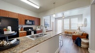 Located at 7803 S New Braunfels Ave in San Antonio, Texas, this single-story residence offers two bedrooms and two bathrooms within a thoughtfully designed floor plan. The open-concept kitchen serves as the heart of the home, featuring rich warm-toned cabinetry, granite countertops, a large peninsula with bar seating, a double basin sink, and black appliances including a refrigerator, range, and microwave. Pendant lighting accents the peninsula, which flows seamlessly into the living area—bright and airy thanks to large windows that invite an abundance of natural light. Wood-style flooring runs throughout, lending a cohesive and modern feel to the space. The bedrooms are comfortably sized with neutral tones, window blinds, and access to closet storage. The bathrooms include granite-topped vanities and a tub-shower combination with tiled surrounds. A dedicated laundry room houses a side-by-side washer and dryer. Additional highlights include multiple closets for storage, hallway connections between rooms for efficient circulation, and a private patio. The overall ambiance is clean, contemporary, and functional—well-suited for everyday living in San Antonio.